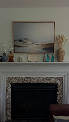 Reviewer's Winter Plains Canvas Art displayed above a fireplace mantel decorated with bottles and a vase.