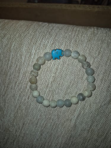 Customer's Expedition Bracelet with light-colored beads and a blue elephant charm on a textured surface.