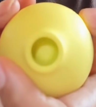Customer's yellow Lem clitoral massager held in a hand, showing the round, smooth shape and central air suction opening.