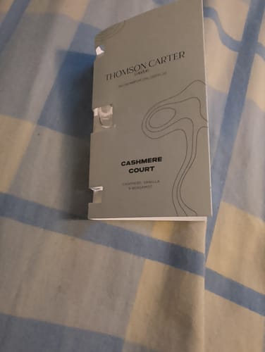 Customer's Cashmere Court perfume sample card featuring elegant branding, resting on a blue and white plaid surface.