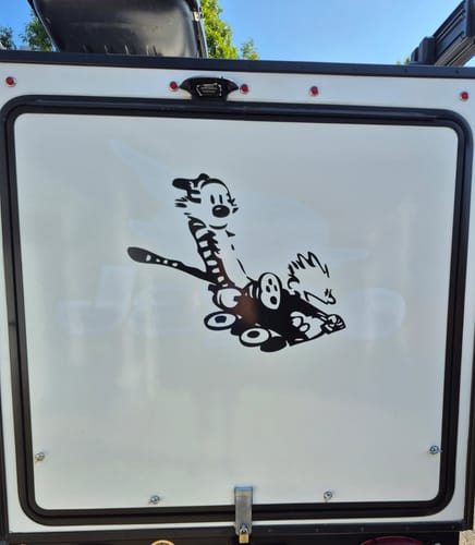 Customer's black Calvin and Hobbes in Wagon decal applied to the rear door of a white travel trailer.