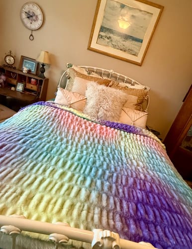 Customer's colorful Hugs Aurora Blanket draped over a bed in a cozy, decorated bedroom.