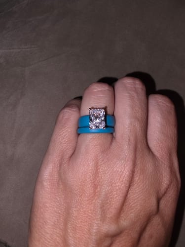 Customer's hand wearing a stack of blue Rinfit silicone wedding rings with a large rectangular gemstone.