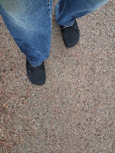 Asiakkaan Vapauta Varpaat -paljasjalkakengät jalassa ulkona asfaltilla sinisten farkkujen kanssa.