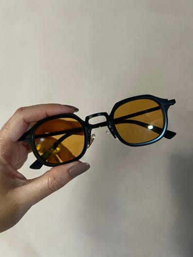 Reviewer's hand holding a pair of Bali sunglasses with a black metal frame and orange-tinted lenses.