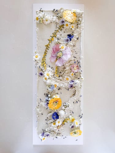 Customer's rectangular cake decorated with vibrant, pressed flowers arranged in a floral table runner design.