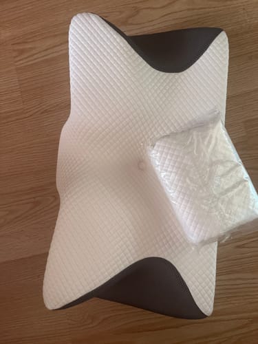 Customer's white and gray Dr.Lumbar Papírtáska ergonomic pillow laying on a wooden floor, with a packaged accessory.