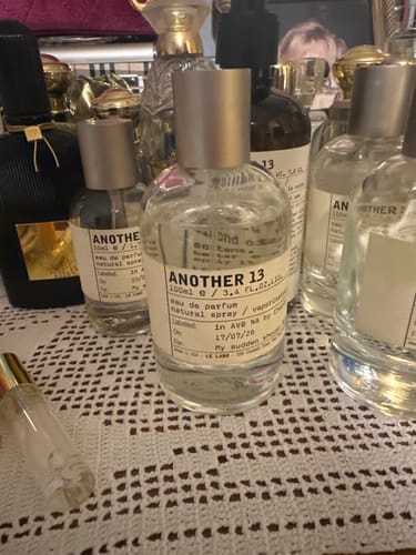 Customer's Another 13 eau de parfum bottles displayed alongside various perfume bottles on a decorative lace surface.