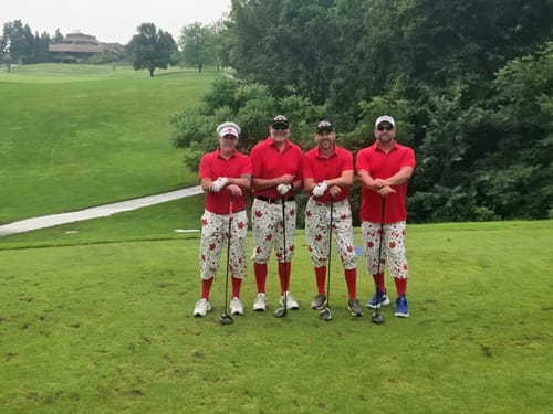 Customer's four golfers in matching red shirts and patterned pants on a green golf course.