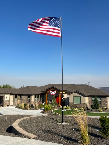 Reviewer's Ultra Heavy Duty American Flag flying on a tall pole outside a house under a clear blue sky.