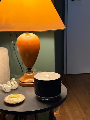Klant's Satori Vulcano Black aroma diffuser in gebruik met zacht licht op een bijzettafel naast een lamp.