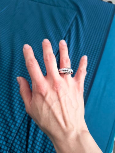Customer's hand wearing the shiny Orbit Plata ring with zirconias on a blue background.