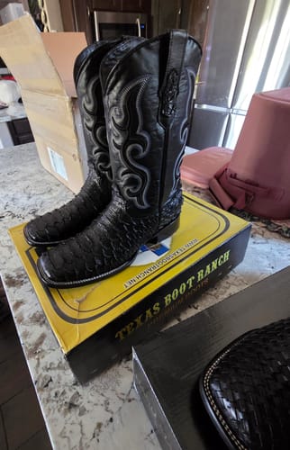 Customer's black python leather boots, featuring square toes and intricate decorative stitching, resting on a box.