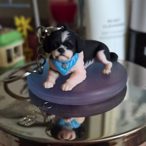 Customer's custom Chibi dog keychain with a black and white coat and blue bandana, placed on a circular display stand.