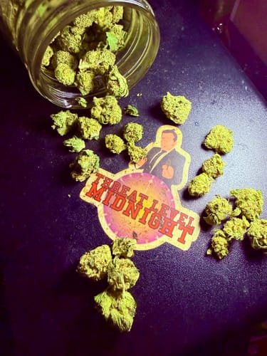Customer's Biscotti THCA Flower small green nugs spilled from a glass jar onto a Threat Level Midnight sticker.
