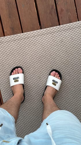 Customer's Prio white slides with black text on feet while wearing light denim shorts on a textured mat.