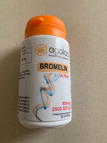 Reviewer's bottle of Bromelin Ultra supplement with orange cap, standing on a neutral surface.