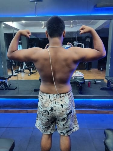 Customer's back profile flexing muscles in a gym setting while using Wellcore Pure Micronised Creatine Monohydrate.