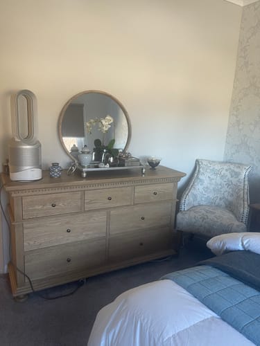 Customer's James Round Mirror with wood frame placed on a bedroom dresser, reflecting decorative items.