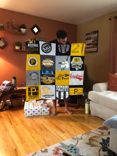Customer's Project Repat T-Shirt Quilt featuring Pittsburgh Pirates logos held up by a person in a living room.