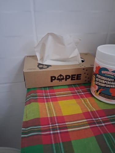 Customer's Popee triple-ply tissue box sitting on a colorful plaid surface, next to a container.