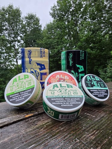 Reviewer's Mountain Wintergreen Nicotine Pouches in several colorful tins and bulk sleeves on a rustic outdoor table.