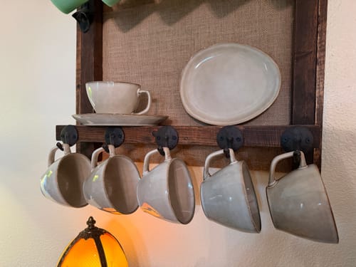 Customer's Crema Large Cup & Saucer set, with several neutral-toned cups hanging on a wall rack and one on a shelf.