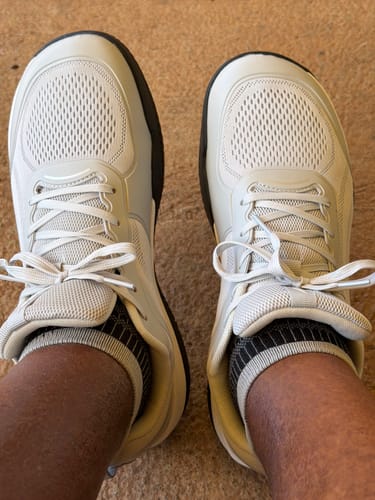 Customer's feet wearing light-colored CUURT Muuv court shoes with wide toe boxes on a ground surface.