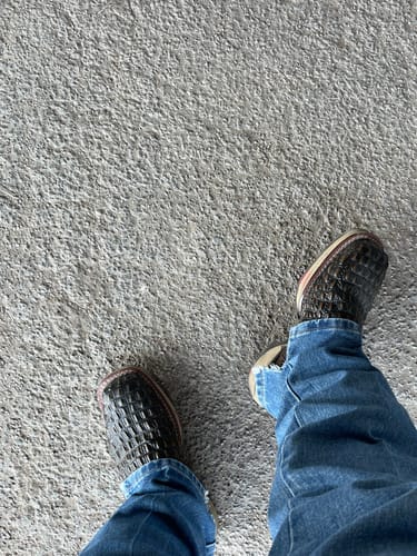 Customer's rustic brown caiman hornback leather boots with square toes worn with blue jeans on concrete.