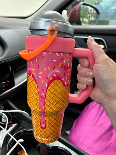 Reviewer's hand holding a pink and yellow ice cream cone themed Mystery Thicc Buddy cup with sprinkles inside a car.