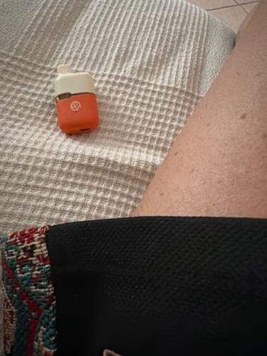 Customer's compact THC-A Vape with a white top and orange body resting on a textured white fabric surface.