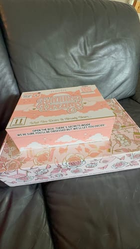 Customer's Fulfilling Dreams Bundle box, resting on a floral patterned base box atop a dark leather sofa.