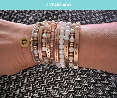 Customer's wrist stacked with several beaded bracelets featuring gold charms and inspirational text engravings.