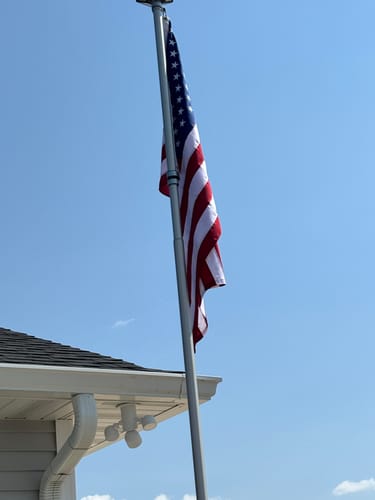 Customer's Ultra Heavy Duty American Flag flying on a pole against a clear blue sky, showing vibrant red, white, and blue.