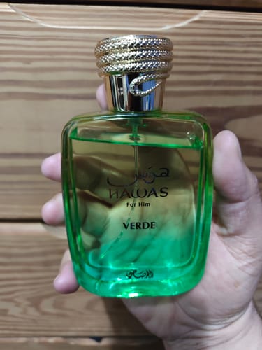 Customer's hand holding a transparent glass bottle of Rasasi Hawas Verde perfume with a textured gold cap