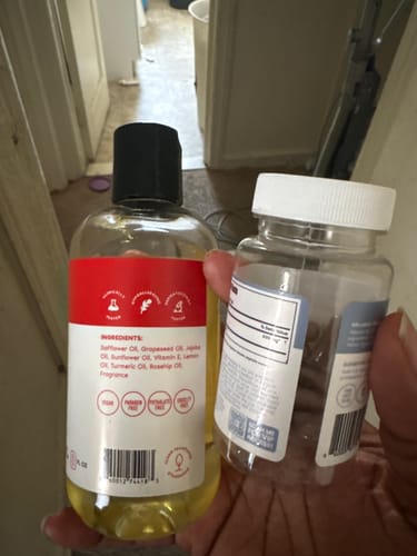 Customer's hand holding a full bottle of oil and an empty supplement bottle from the Moisture Support + Hydration Kit.