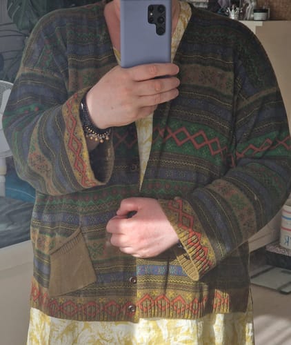 Reviewer taking a mirror selfie in the geometric knitted V-neck sweater, worn open to show the colorful pattern.