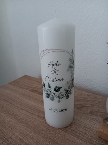 Rezensent zeigt die personalisierte Hochzeitskerze 'Floral Kreis' mit den Namen Anke & Christian auf einem Holztisch.