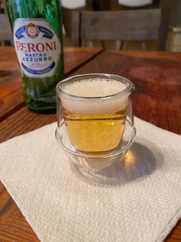 Reviewer's double wall espresso cup filled with a light, foamy beverage on a wooden table.