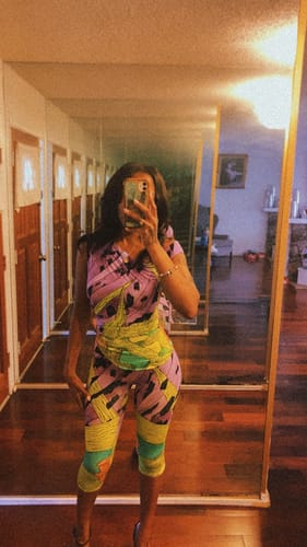 Reviewer taking a mirror selfie in a hallway wearing the colorful Naked Print Capri Legging and a matching top.