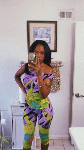Reviewer posing in a bathroom wearing the Naked Print Capri Legging and a matching off-the-shoulder top.