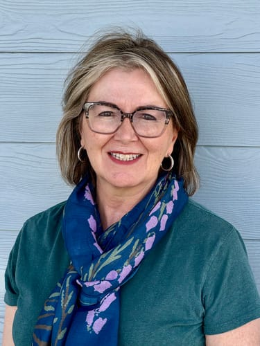 Reviewer smiling while wearing the navy blue Larkspur All-Season Scarf with a purple floral print.