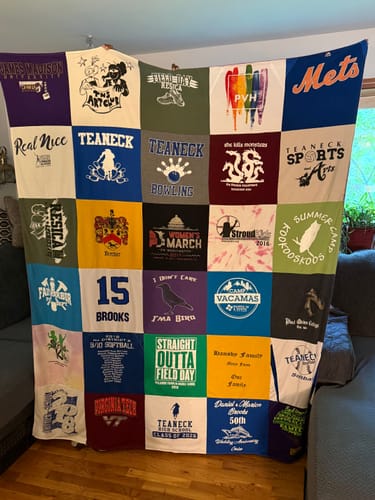 Customer holding up their finished Premium T-Shirt Quilt, a colorful grid made from memorable t-shirts.