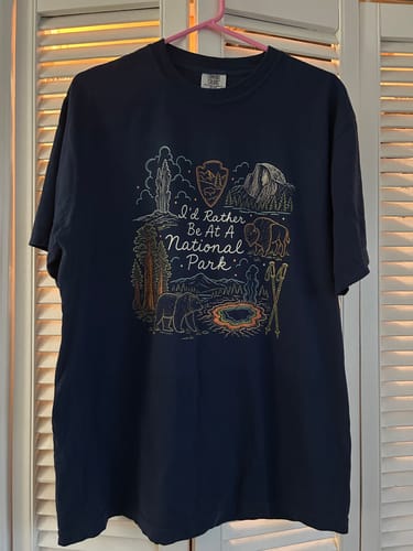 Customer's navy blue 'I'd Rather Be At A Park T-Shirt' hanging up, showing the detailed national park-themed graphic.