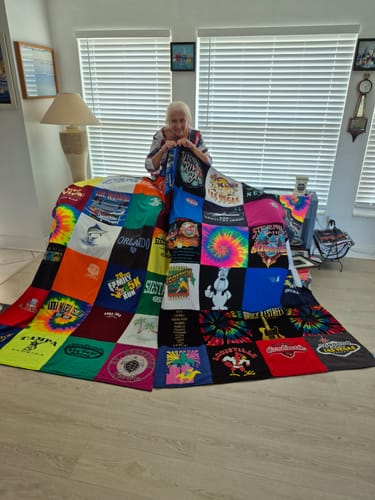 A customer holds up a large Project Repat T-Shirt Quilt made of many colorful t-shirt squares.