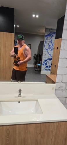 Reviewer in a gym mirror flexing their bicep to show muscle pump after using UGLYFACE® HYDROPRIME®.