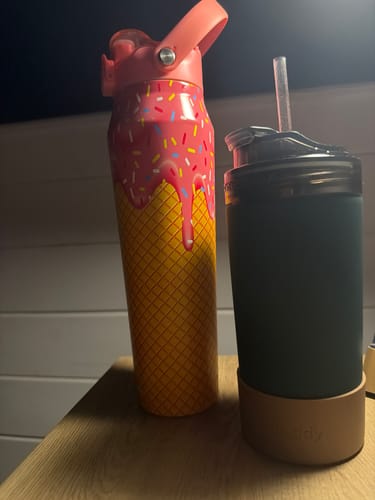 Reviewer's dark green Emerald Elegance Universal XL bottle on a wooden table next to another colorful bottle.