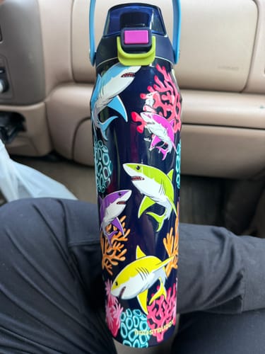Customer's Bottle Buddy 32oz in Neon Coast design, with colorful sharks, held on a person's lap in a car.