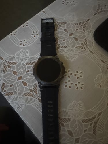 Customer's black Gard Pro Ultra 2+ smartwatch with a dark screen, lying on a patterned tablecloth.