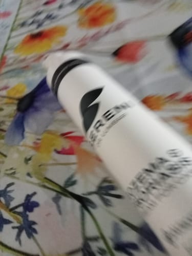Customer's blurry, close-up shot of the white Sereni Pikkelysömör és Ekcéma Krém bottle on a floral surface.